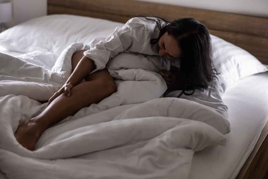 Mulher com espasmo muscular intenso na panturrilha durante a noite em quarto escuro.