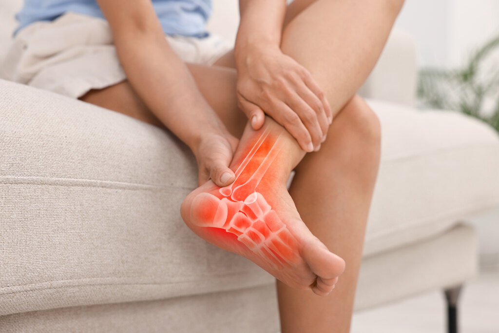 Mulher com dor intensa no pé e articulações associada à fragilidade óssea, osteopenia e saúde óssea comprometida.